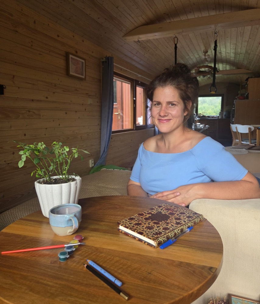 Barbora Štěpánková u kulatého dřevěného stolu, na němž leží zápisník, pastelky a barvy